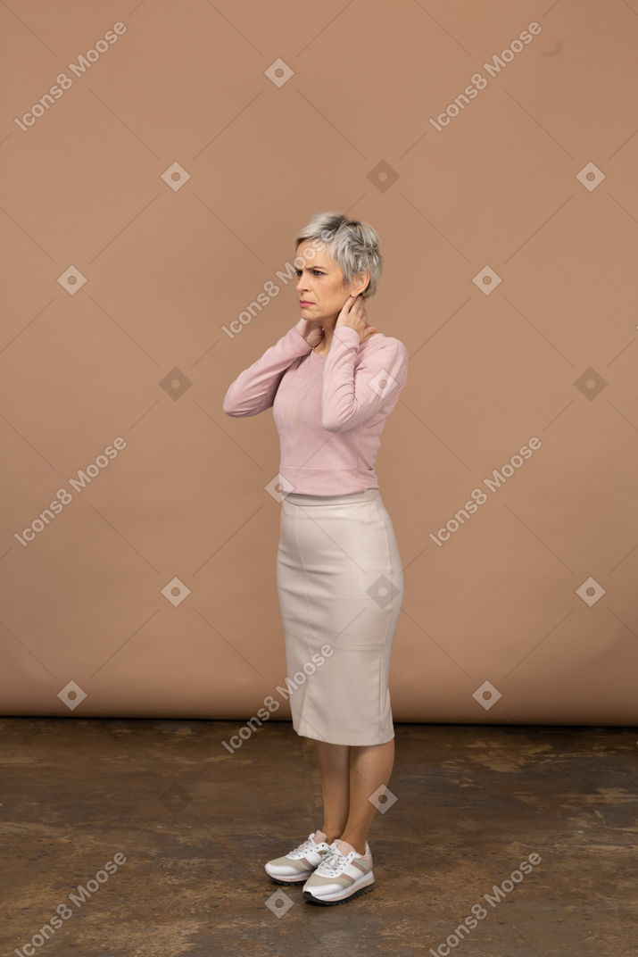 Vue latérale d'une femme en vêtements décontractés debout avec les mains derrière la tête