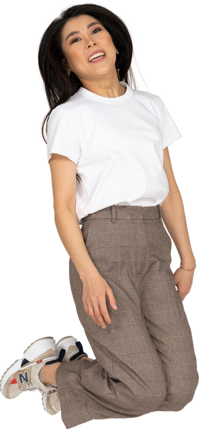 Vista frontal de uma jovem saltitante de calça e camiseta dobrando os joelhos