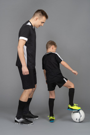 De cuerpo entero de un joven entrenando a un niño pequeño cómo jugar fooyball