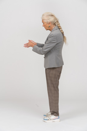 Vista lateral de una anciana en traje mostrando algo
