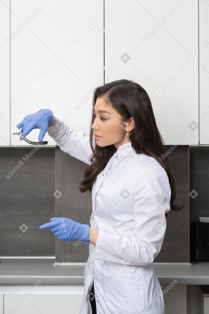 Side view of a female doctor raising hand and holding dental instruments while looking aside