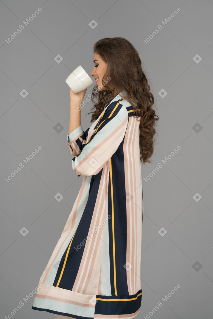 Hermosa mujer árabe de pie de lado y bebiendo de una taza blanca