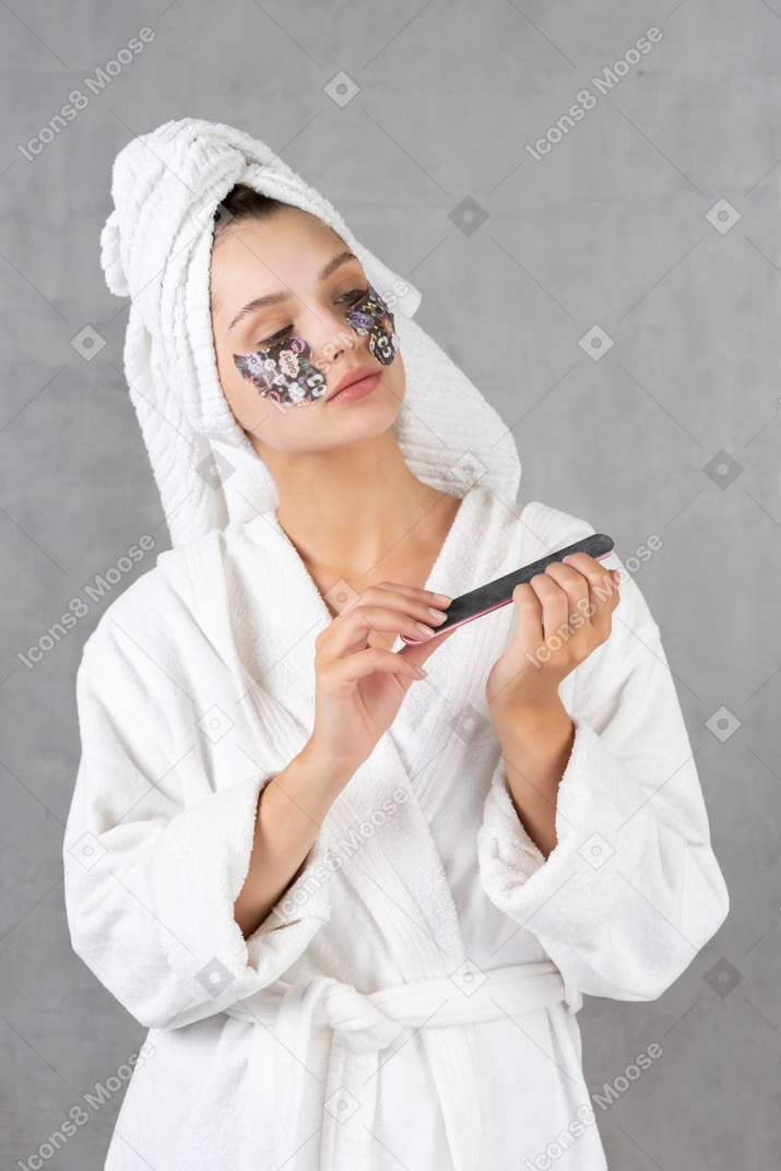 Mujer en bata de baño limandose las uñas