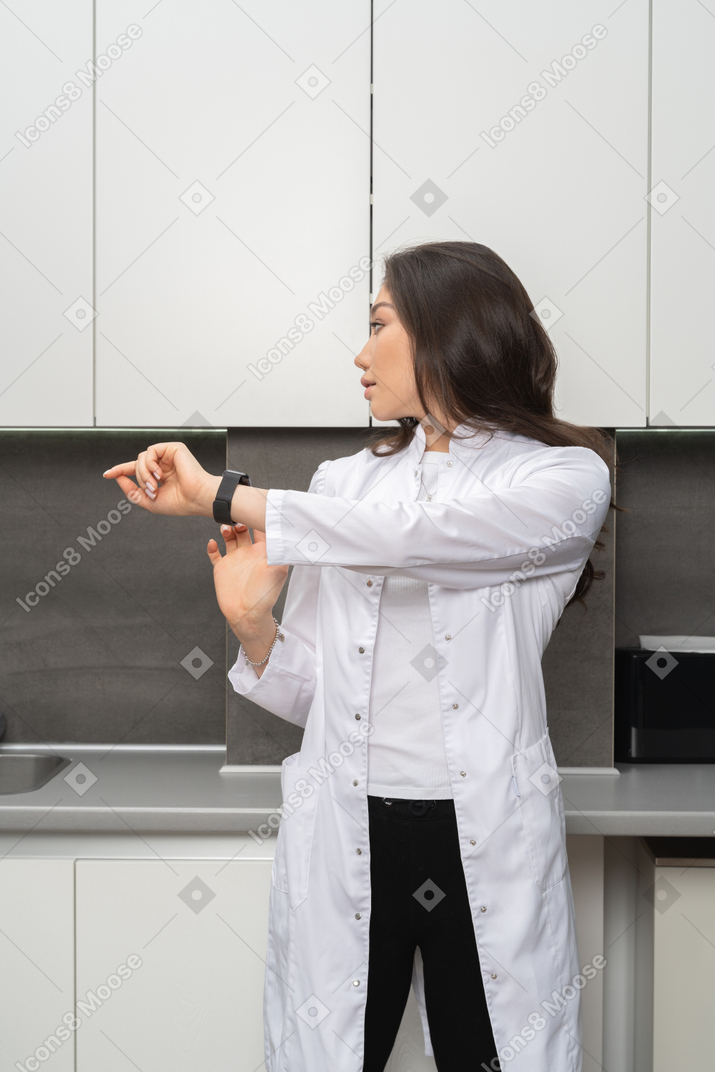 Woman in white lab coat pointing at her watch