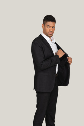 Vista lateral de um jovem de terno preto colocando algo no bolso
