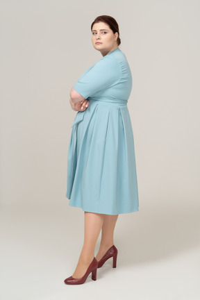 Вид сбоку женщины в синем платье позирует со скрещенными руками