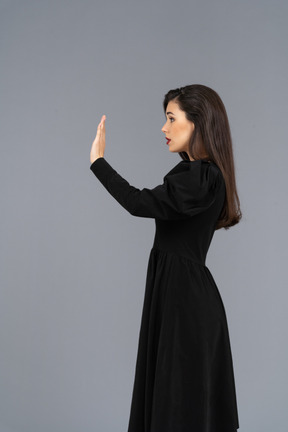 Seitenansicht einer jungen dame in einem schwarzen kleid, die ihre hand hebt