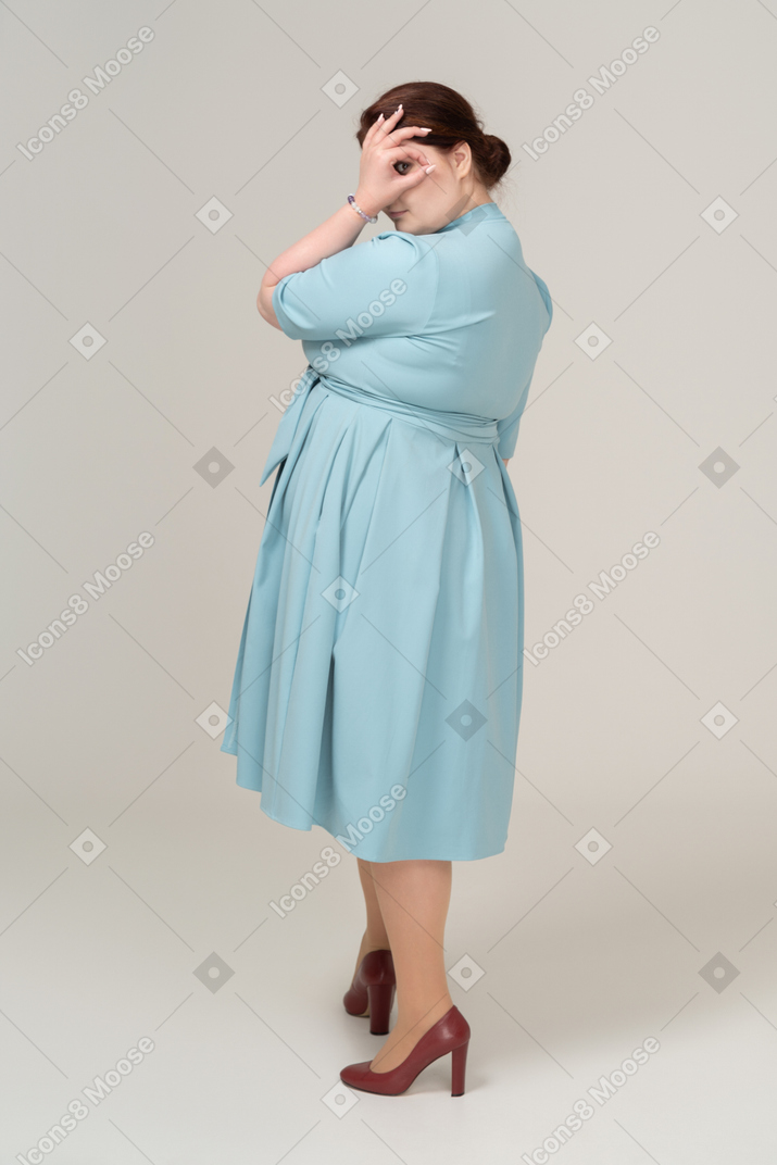 Vue latérale d'une femme en robe bleue regardant à travers les doigts