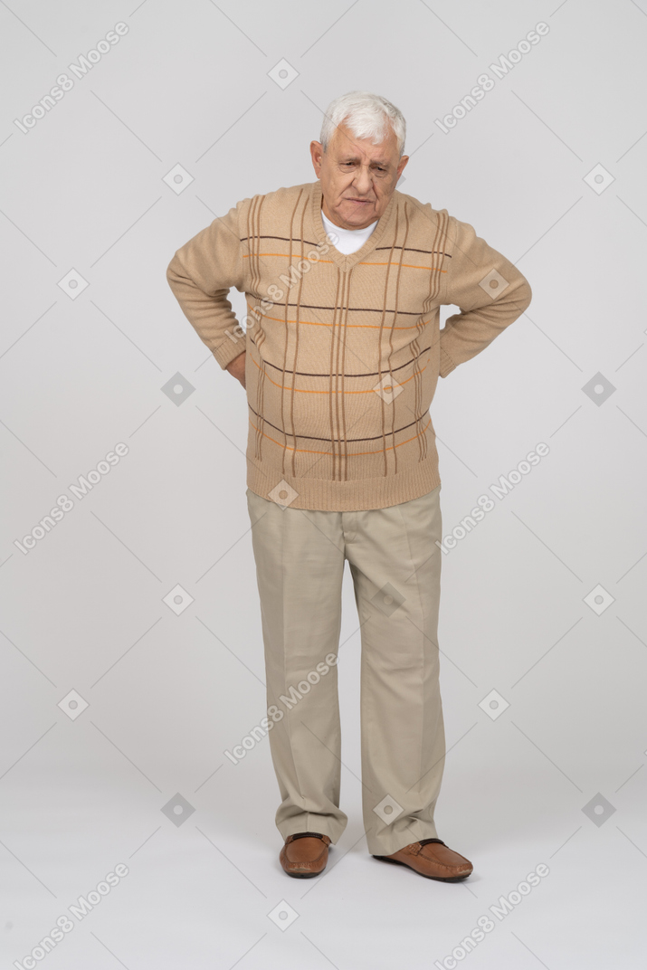 Front view of an old man in casual clothes standing with hands on back
