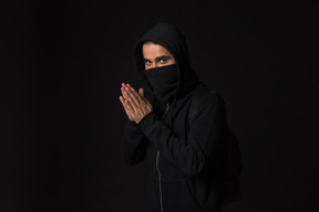 Hacker guy with covered face standing in the dark with hands folded