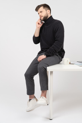 Frown office worker sitting on white desk and talking on the phone