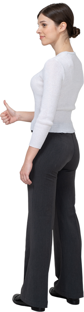Vista posteriore di tre quarti di una giovane donna allegra in abiti da ufficio che mostra il pollice in su