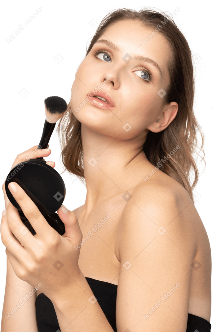 Vue latérale d'une jeune femme appliquant de la poudre pour le visage tout en tenant un miroir