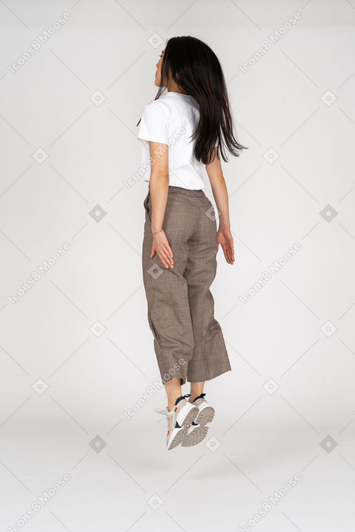 Vista traseira de três quartos de uma jovem saltitante de calça e camiseta