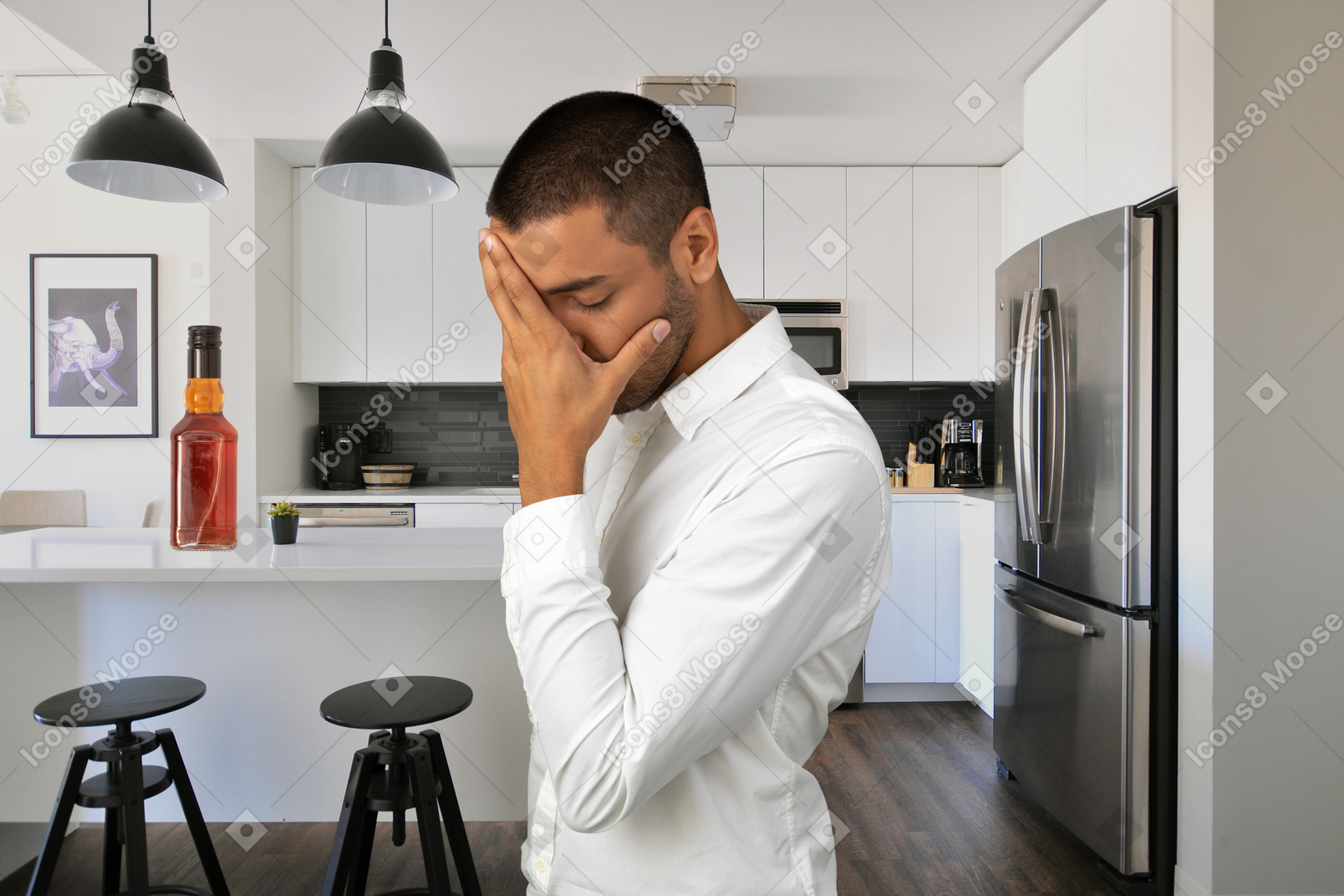 A man standing in a kitchen holding his head