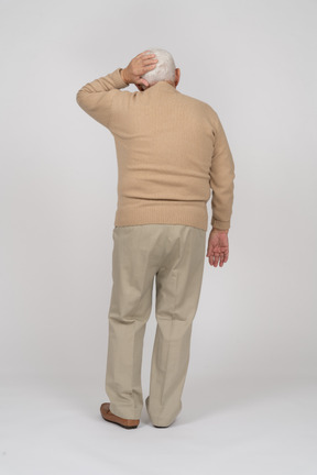 Rear view of an old man standing with hand on head