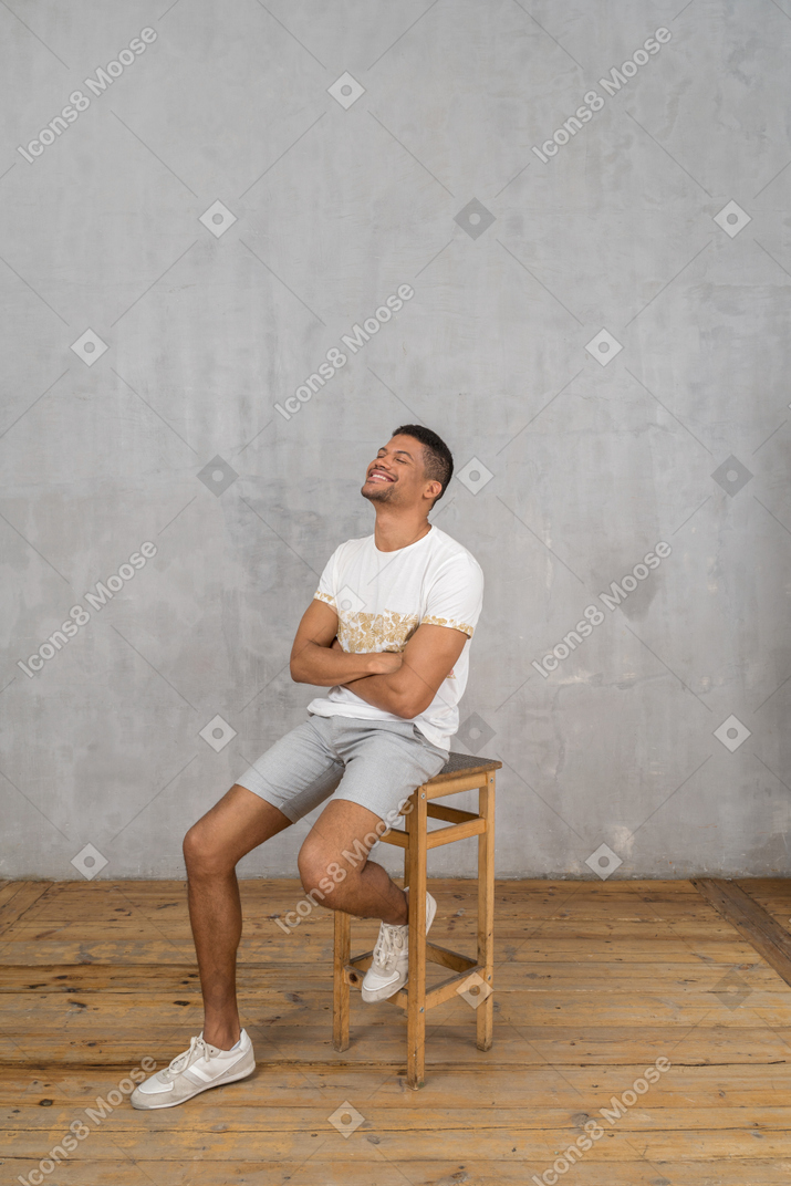 Hombre sonriente sentado con los brazos cruzados y mirando hacia arriba