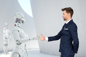 一个时尚的男人握着女人机器人的手，而另一个女人机器人正等着她