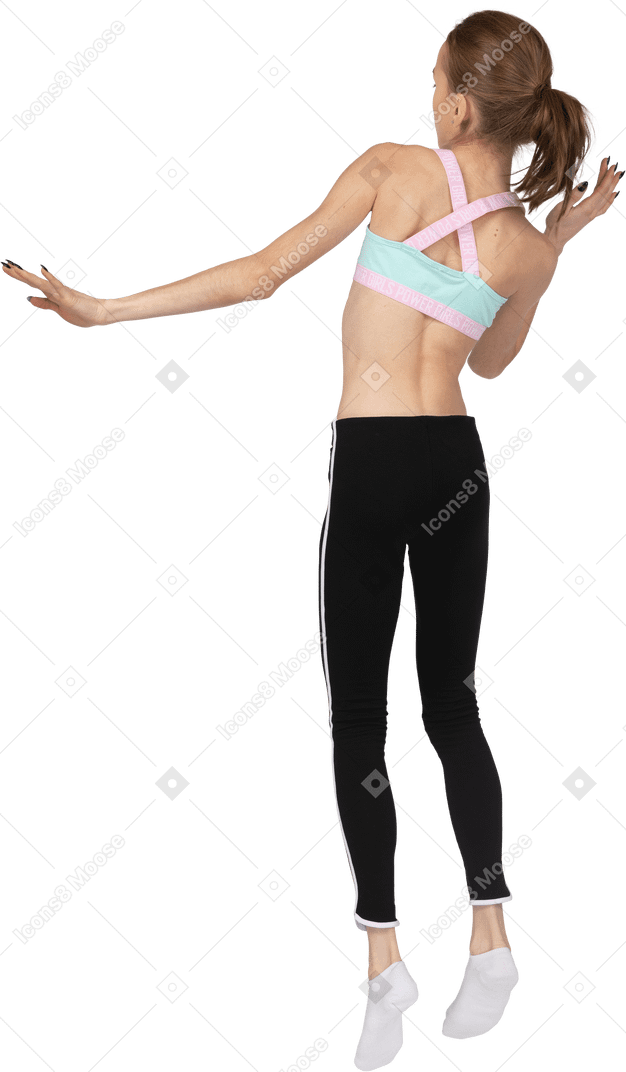 Vista traseira de três quartos de uma adolescente em roupas esportivas levantando a mão e pulando