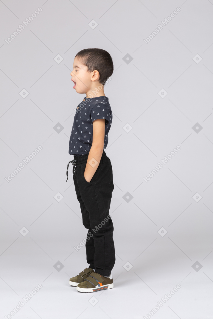 Vista lateral de un niño dormido de pie con las manos en los bolsillos y bostezos