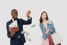 Excited girl holding shopping bags and man throwing money bills