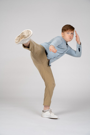 A young boy in a blue shirt and khaki pants is doing a kick