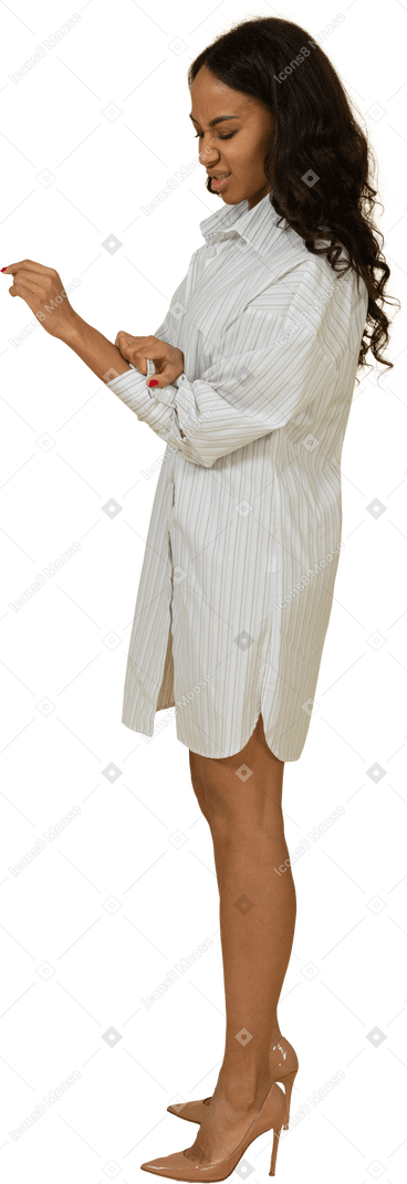 Vista lateral de uma jovem mulher de pele escura irritada em um vestido branco abotoando a manga