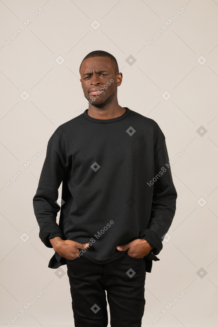 Confused young man standing with his hands in his pockets