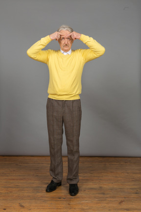 Vista frontal de un anciano perplejo en jersey amarillo gesticulando activamente y mirando a la cámara