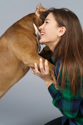 Vista laterale di una donna sorridente in camicia a quadri che abbraccia il suo bulldog