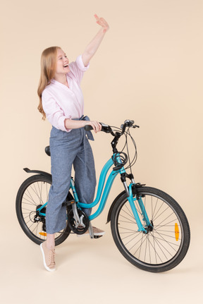 Happy young woman riding on bicycle and waving with a hand