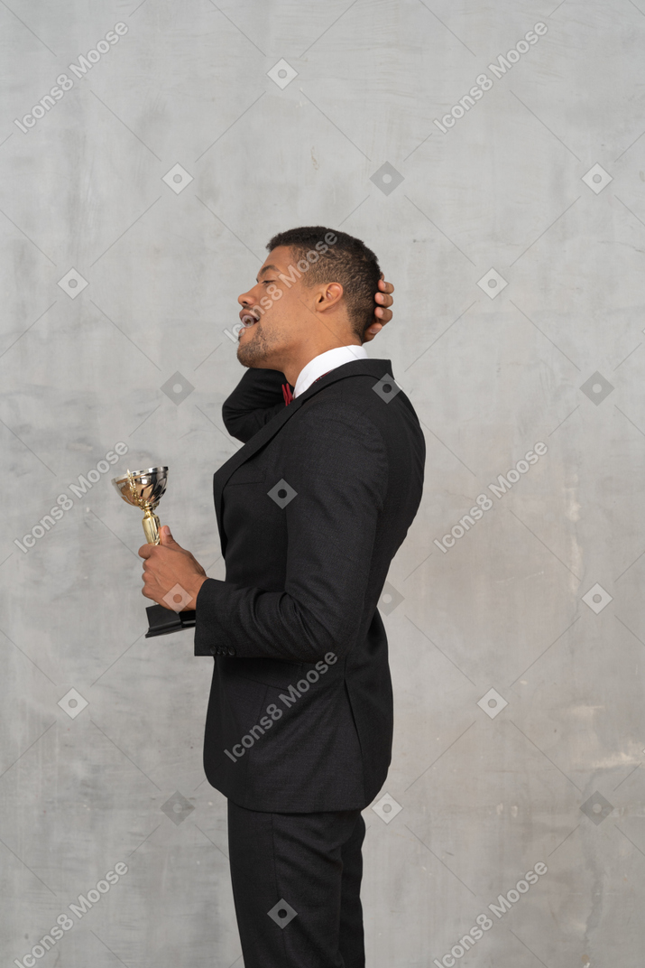 Vista lateral de un hombre de traje sosteniendo un premio.
