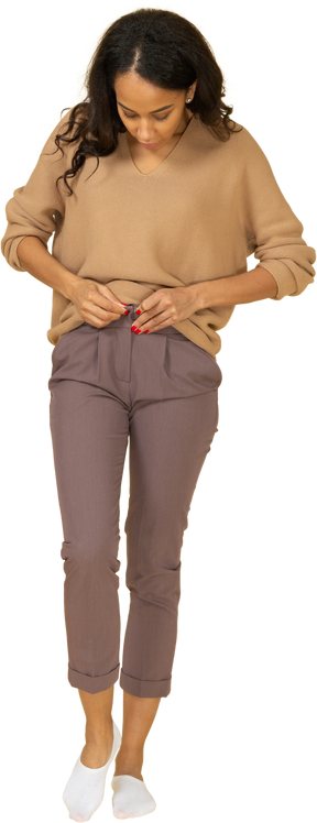 Vista frontal de una mujer joven de piel oscura subiendo la cremallera de sus pantalones