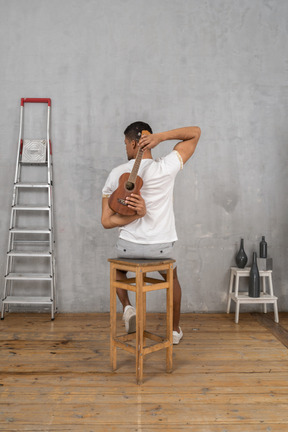 Back view of a man on a stool holding an ukulele behind his back