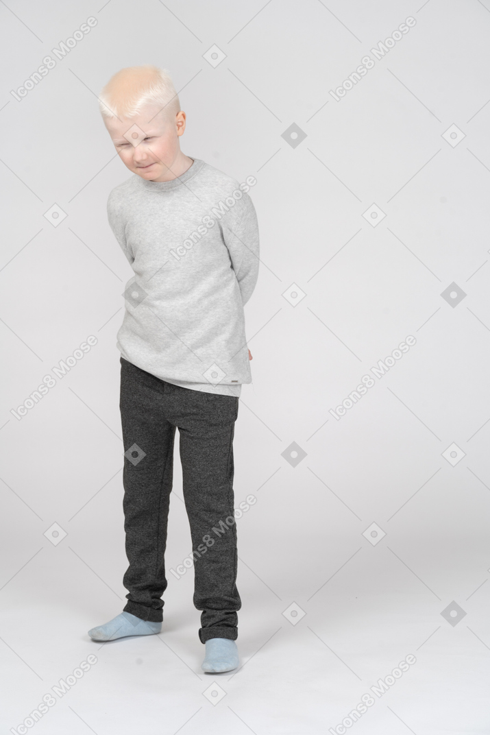 Front view of a sly suspicious kid boy hiding hands behind
