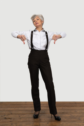 Front view of an old displeased female in office clothes showing a thumb down with both hands