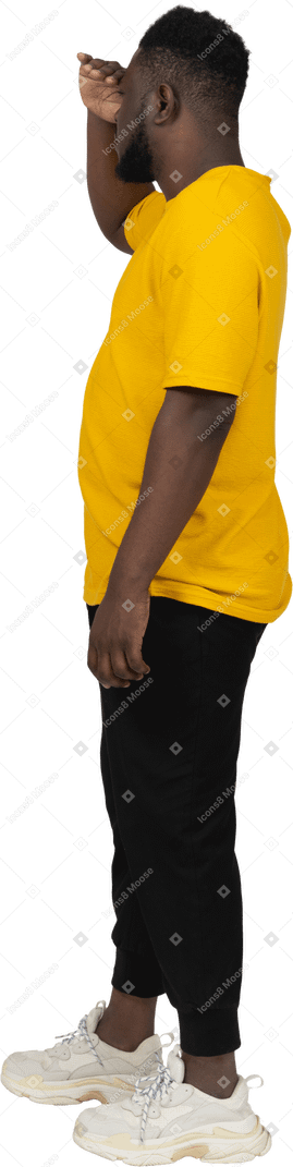 何かを探している黄色のtシャツを着た若い浅黒い肌の男の側面図