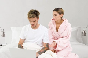 A man and a woman sitting on a bed with laptop