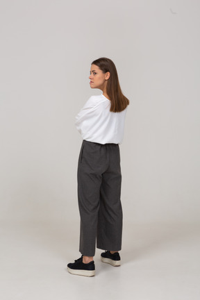 Three-quarter back view of an angry young lady in office clothing crossing arms