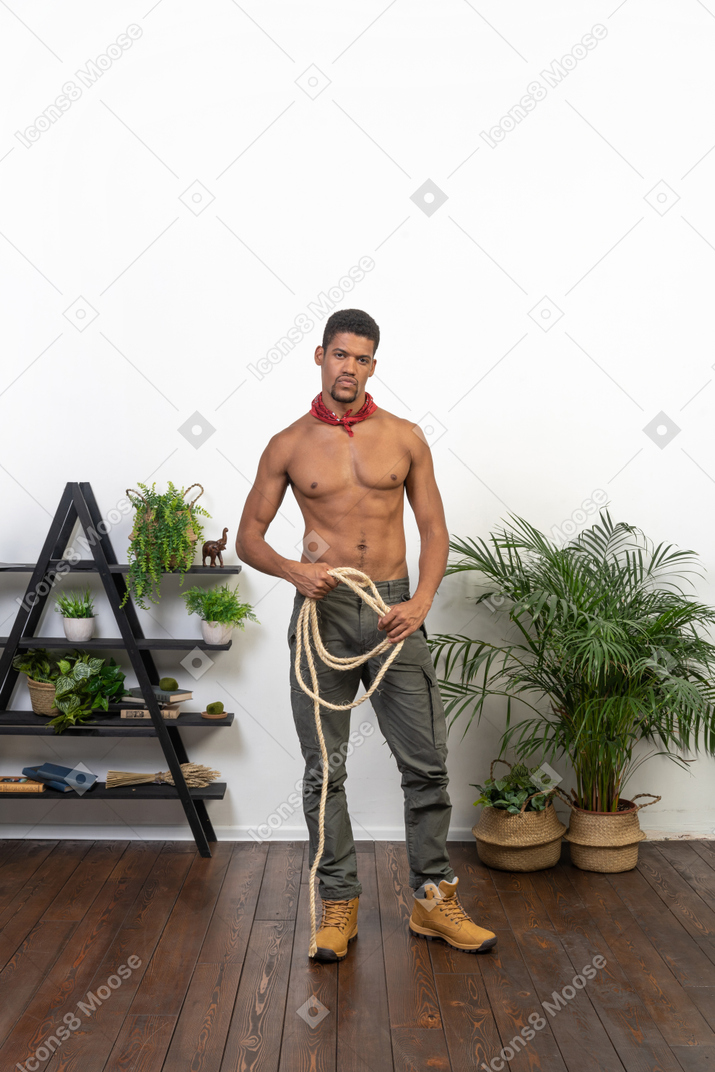 Front view of young man standing and holding a coil of rope and looking at camera
