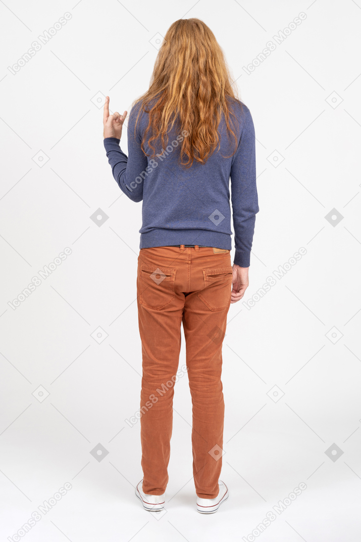 Rear view of a young man in casual clothes making rock on gesture