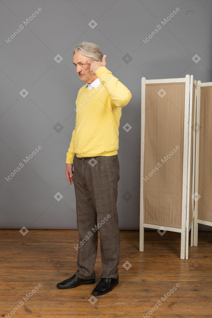 体贴的老人，在黄色的套衫，指着他的头的四分之三的视图