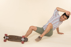 A nice-looking caucasian guy in a striped t-shirt, having fun learning how to ride a skateboard