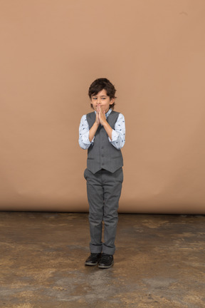 祈りのジェスチャーをしている灰色のスーツを着た少年の正面図