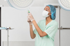 A woman in scrubs and a surgical mask holding a syringe