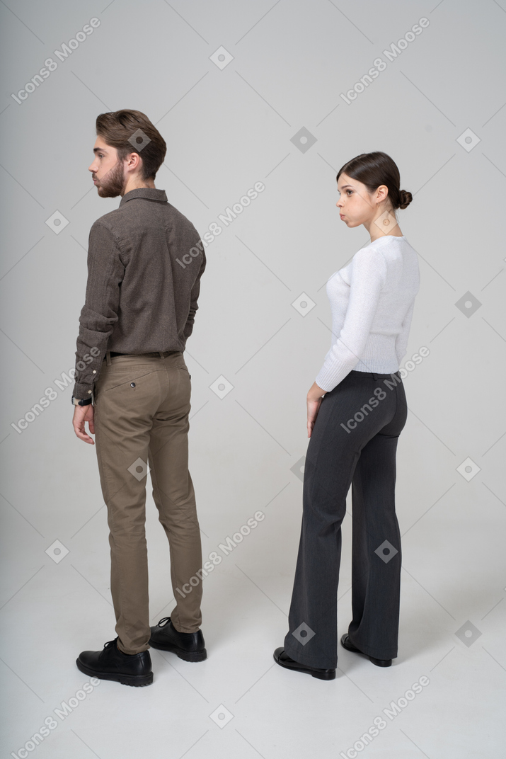 Vista posteriore di tre quarti di una giovane coppia in abiti da ufficio che soffia sulle guance