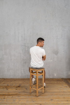 Vista trasera del joven sentado y mirando a un lado