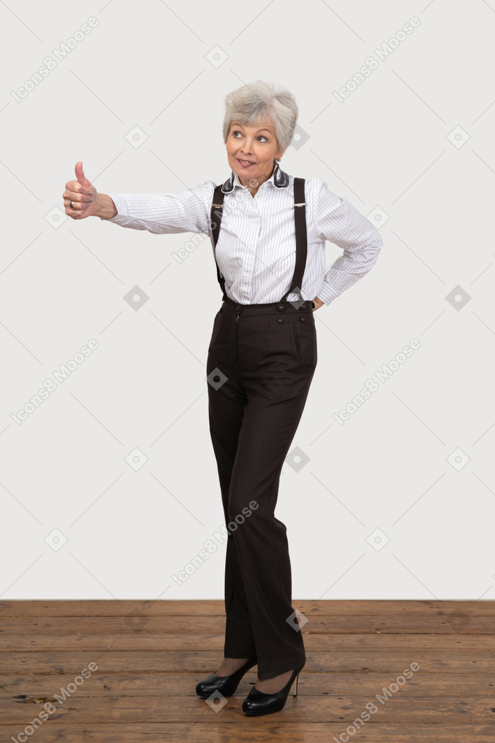 Three-quarter view of an old lady in office clothing putting thumb up