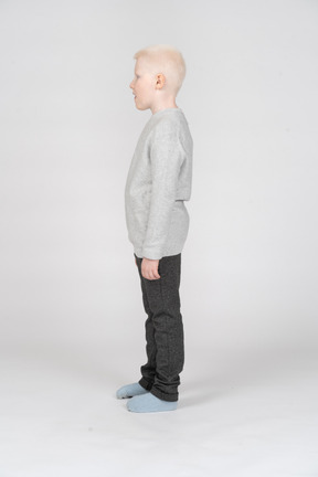 Vista lateral de um garoto garoto com roupas casuais olhando para o lado e mostrando a língua