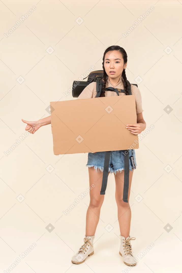 Jeune auto-stoppeur femme tenant une carte de papier et montrant le pouce vers le haut